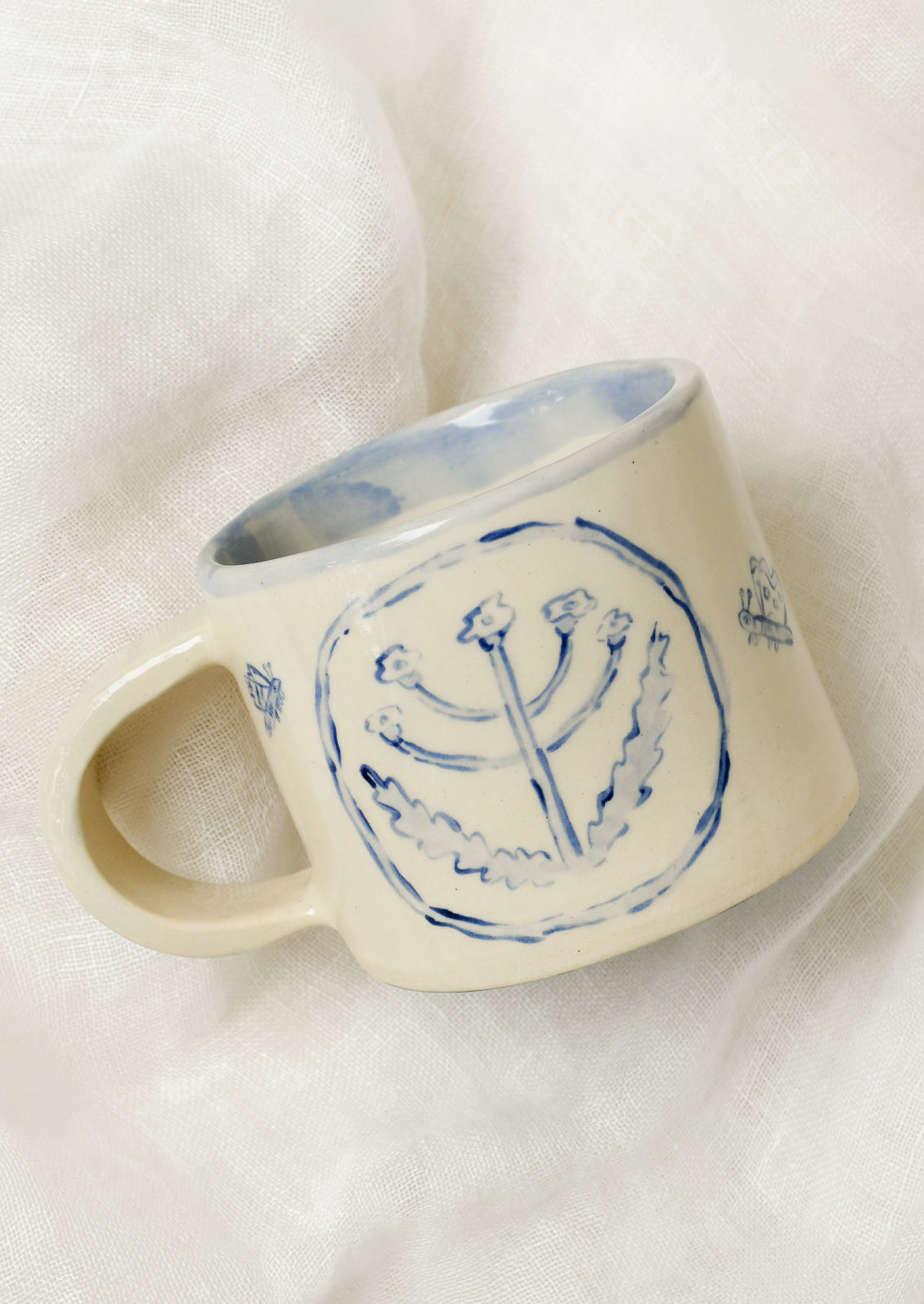 A handmade ceramic mug with illustrations of flowers and tiny insects on the outside and a gingham pattern on the inside.