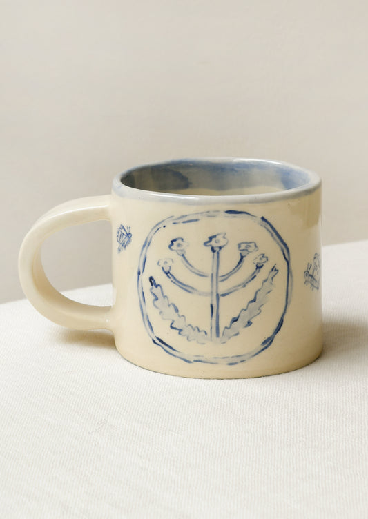 A handmade ceramic mug with illustrations of flowers and tiny insects on the outside and a gingham pattern on the inside.
