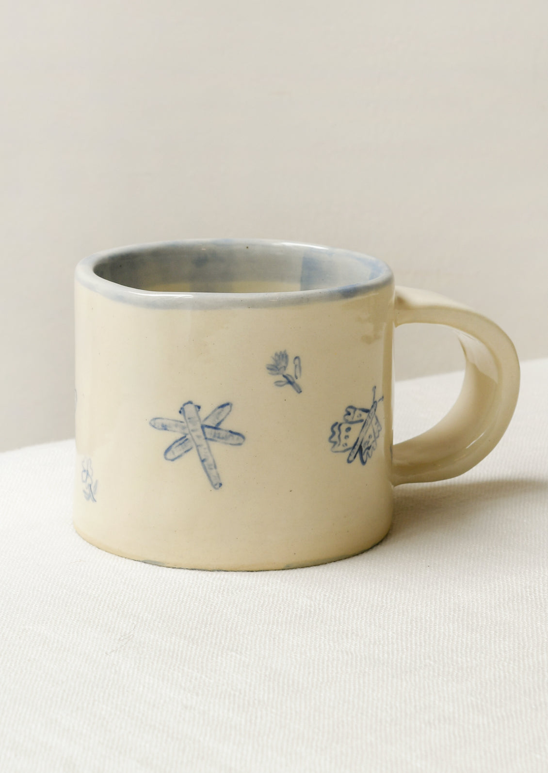 A handmade ceramic mug with illustrations of flowers and tiny insects on the outside and a gingham pattern on the inside.
