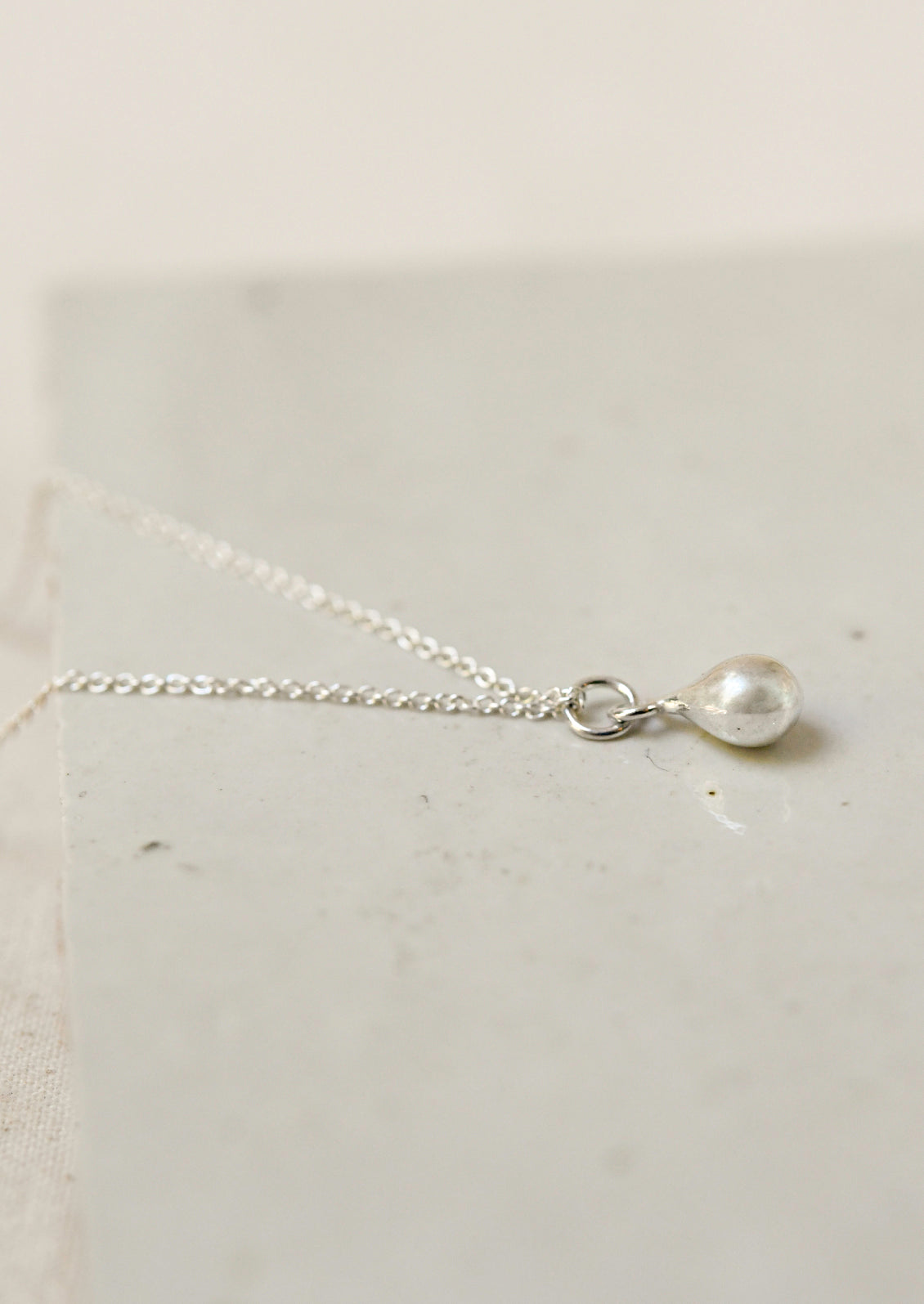 A sterling silver necklace with a dew drop shaped charm.