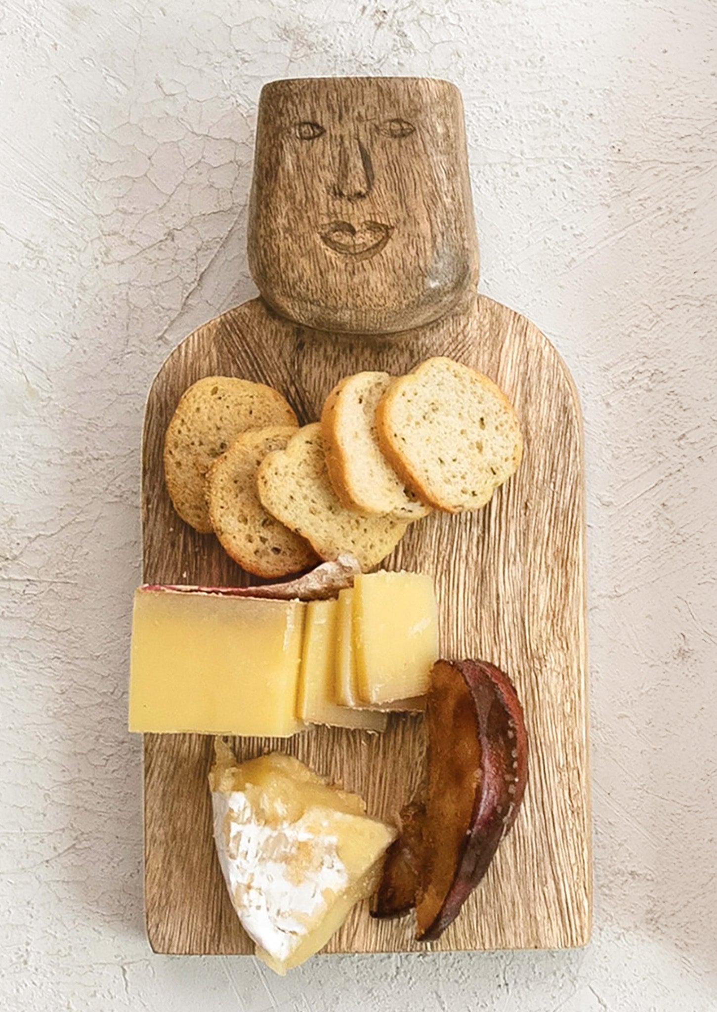 A small wooden serving board with a face carved into the handle.