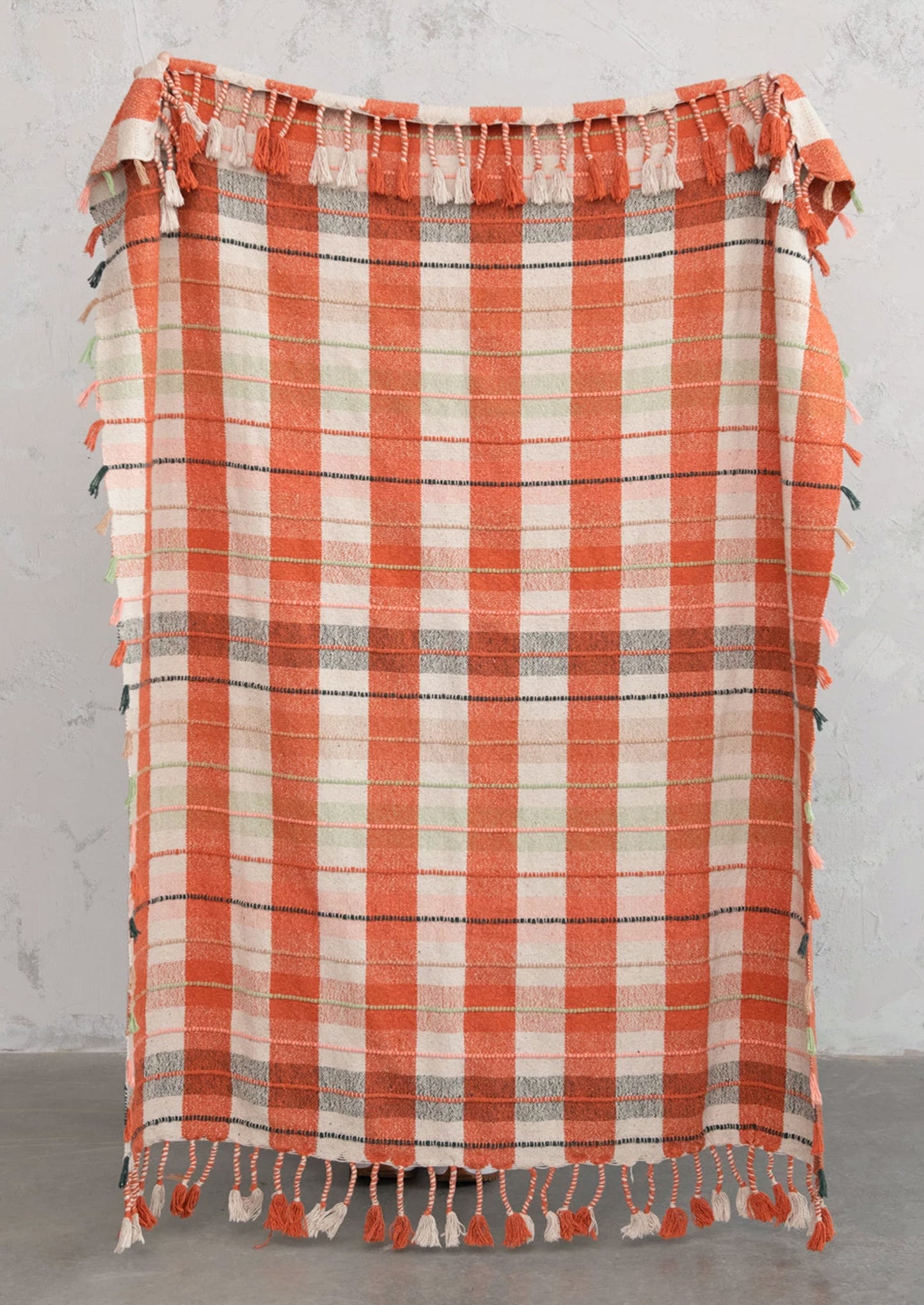 A cotton blend throw blanket in orange and cream plaid with multicolor tasseled stripe detailing.