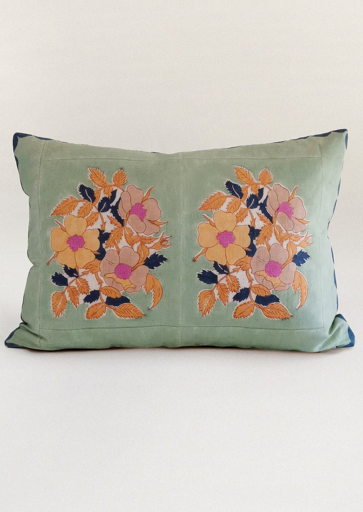 A block printed throw pillow in mint green with orange floral print.