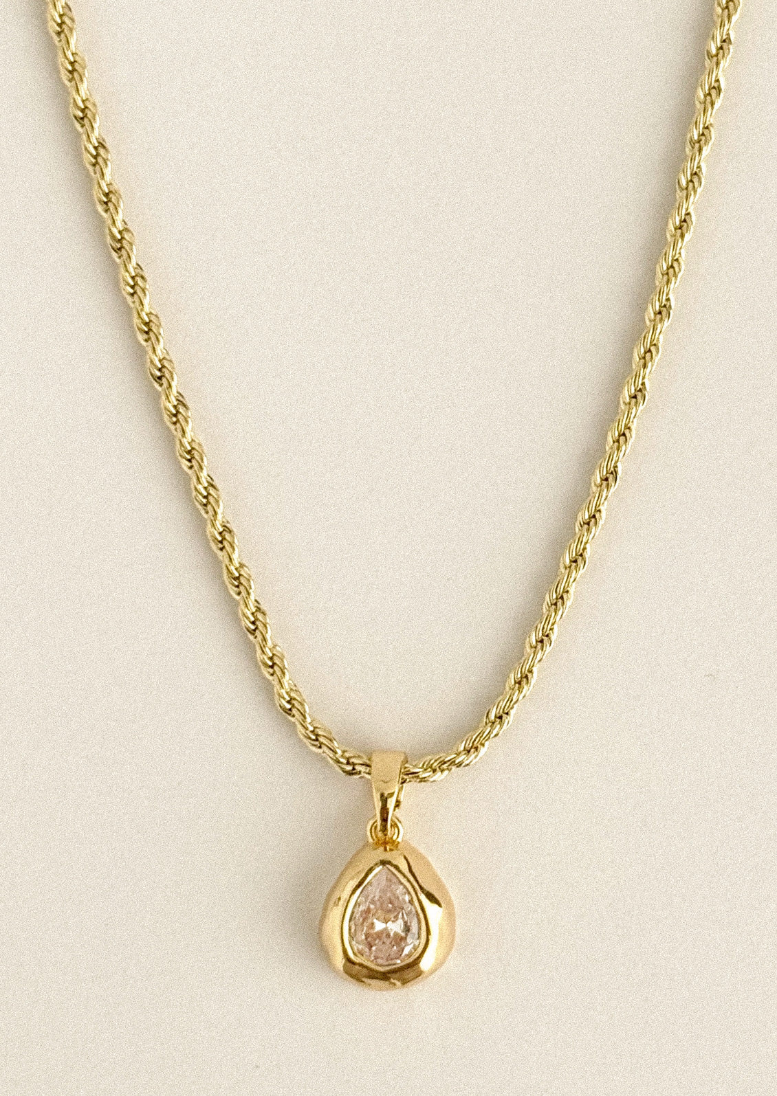 A gold necklace with a teardrop crystal charm.