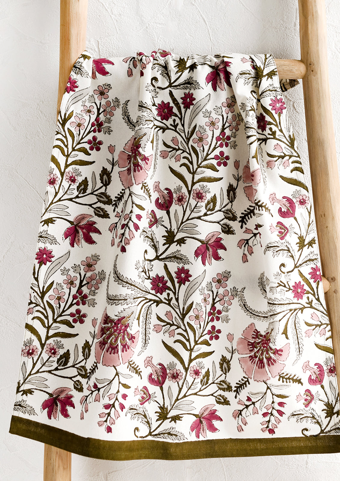 A cotton tea towel in block printed floral pattern in maroon, mauve and olive green.