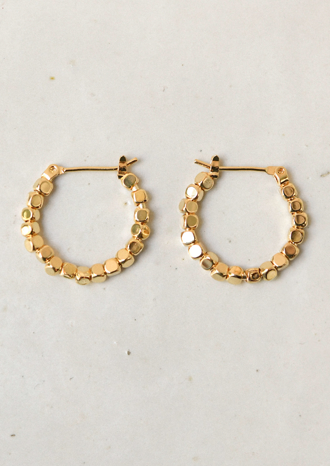 A pair of shiny gold hoop earrings made of gold beads.