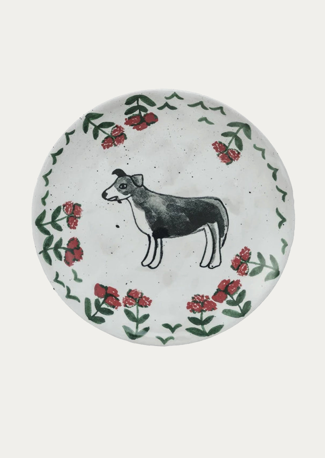 A small ceramic plate with hand painted imagery of black and white dog with red flowers.