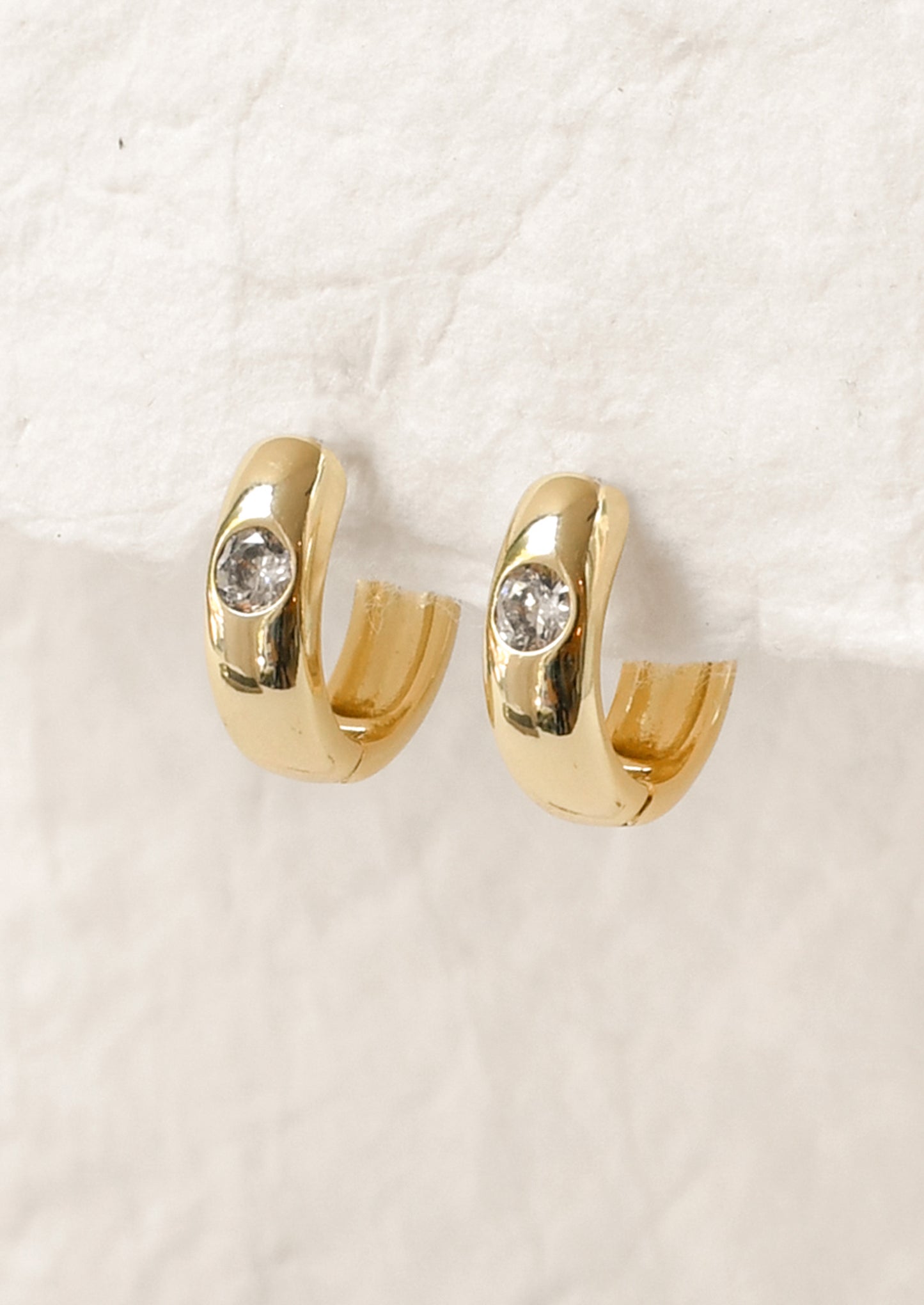 A pair of gold hoop earrings with a round diamond on the front.