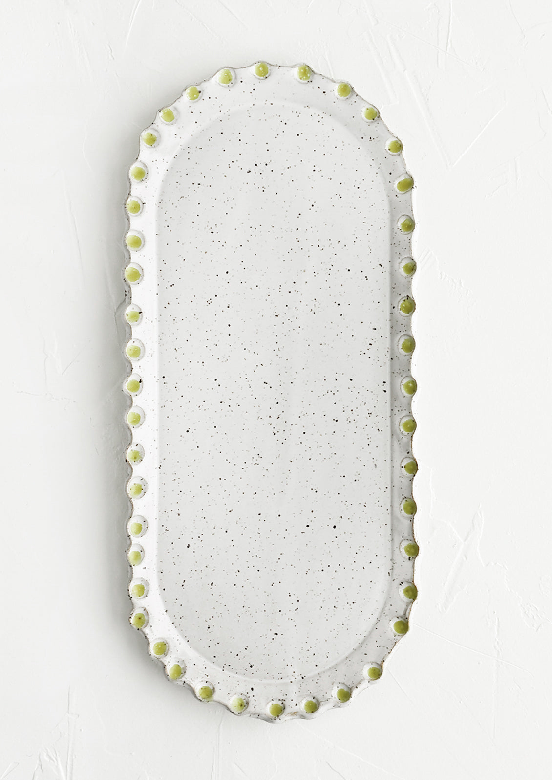 An oblong, oval shaped ceramic platter with green dot imprint border.