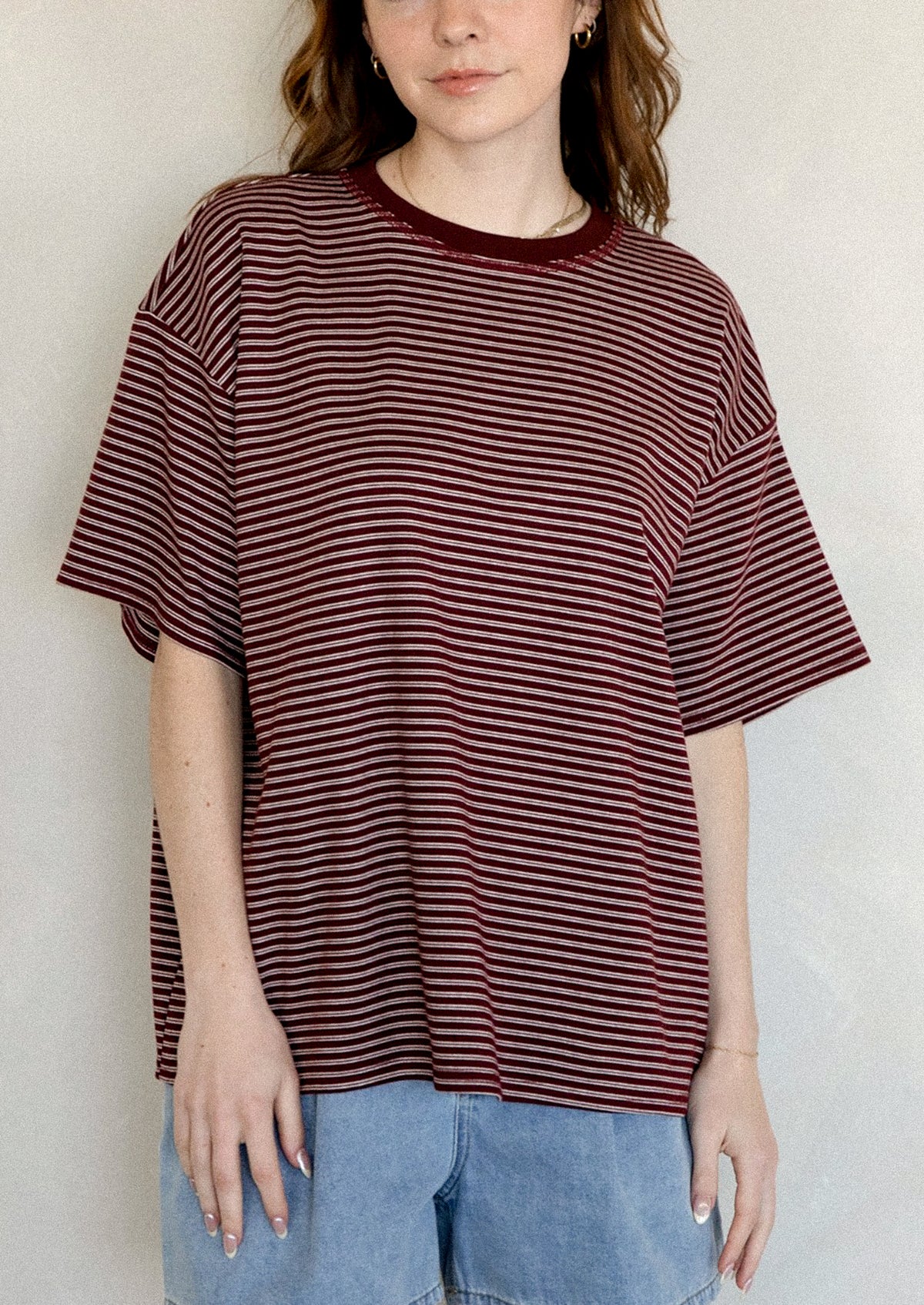 A person wearing an oversized t-shirt in maroon with white stripes.