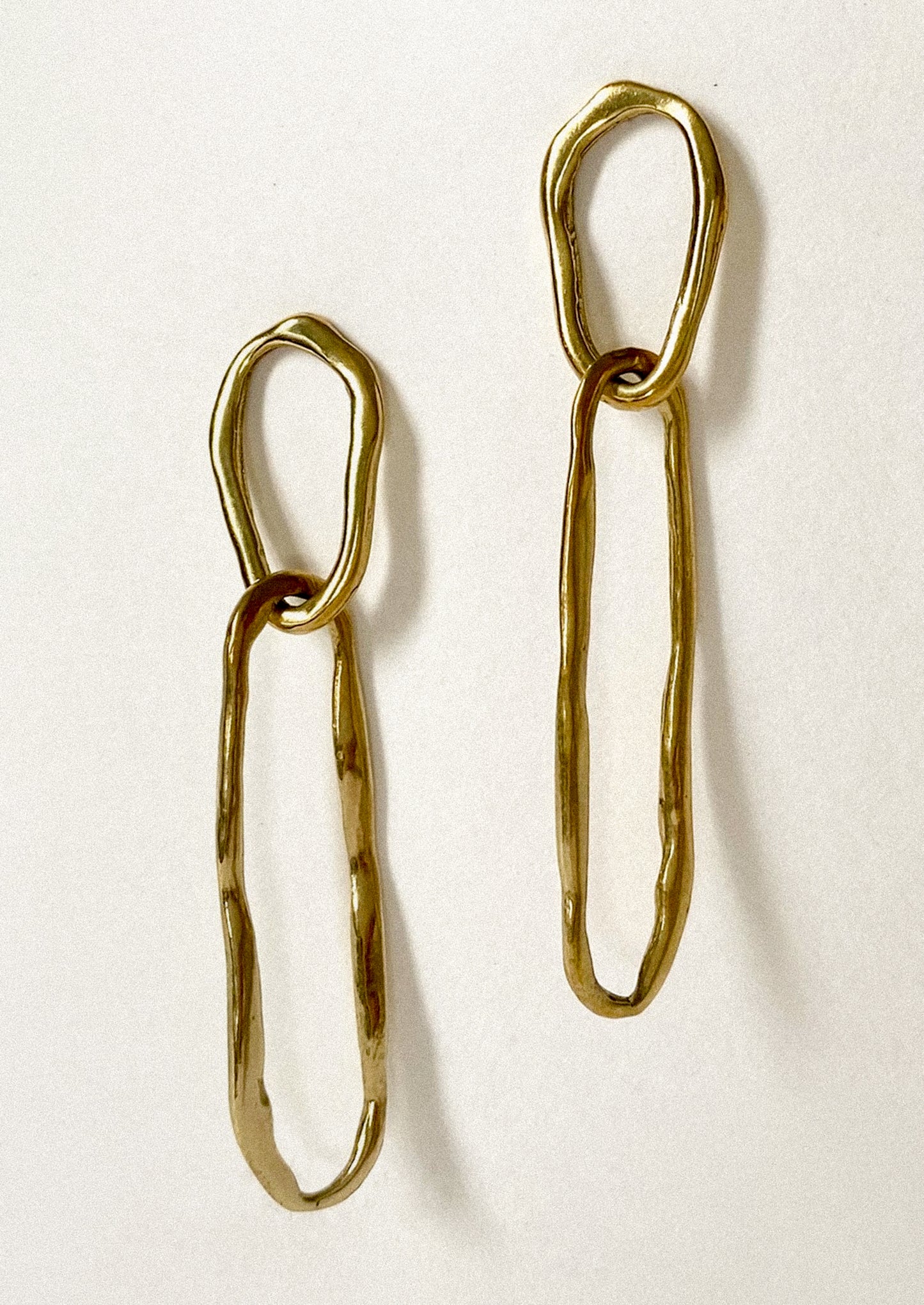 A pair of brass earrings with two amorphous link shapes connected.