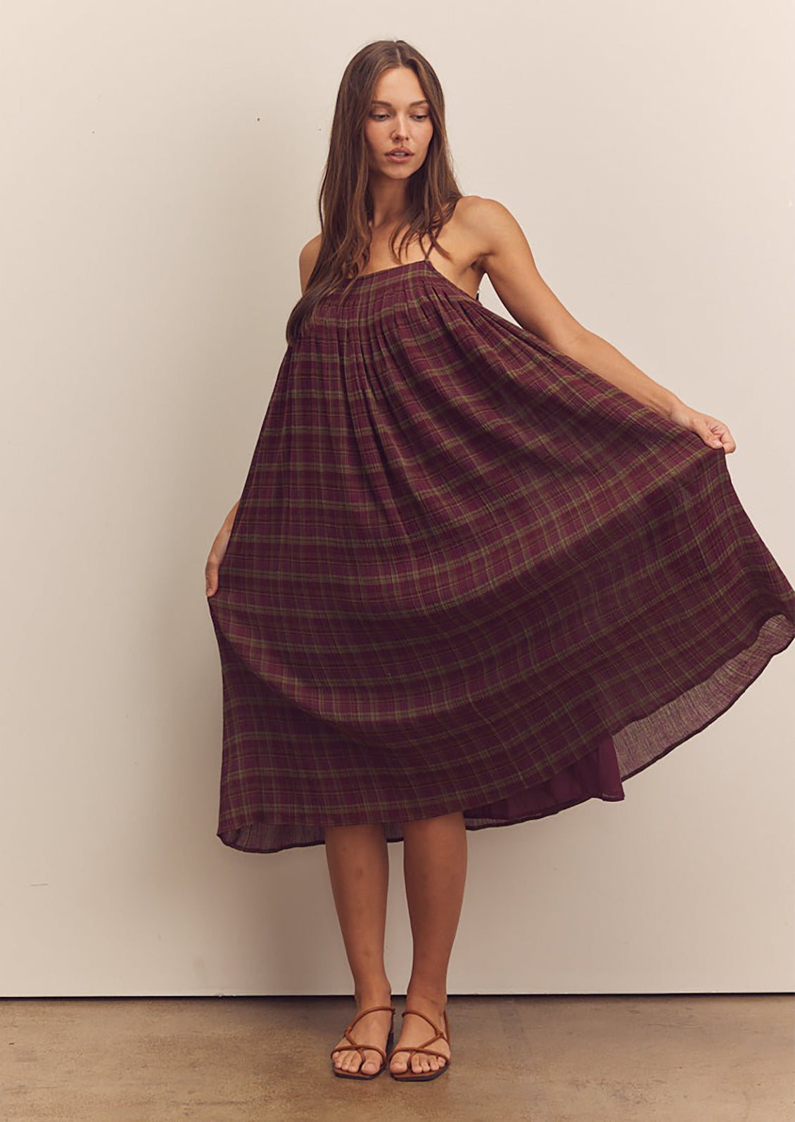 A person wearing a midi length dress in burgundy and green plaid pattern with thin straps.
