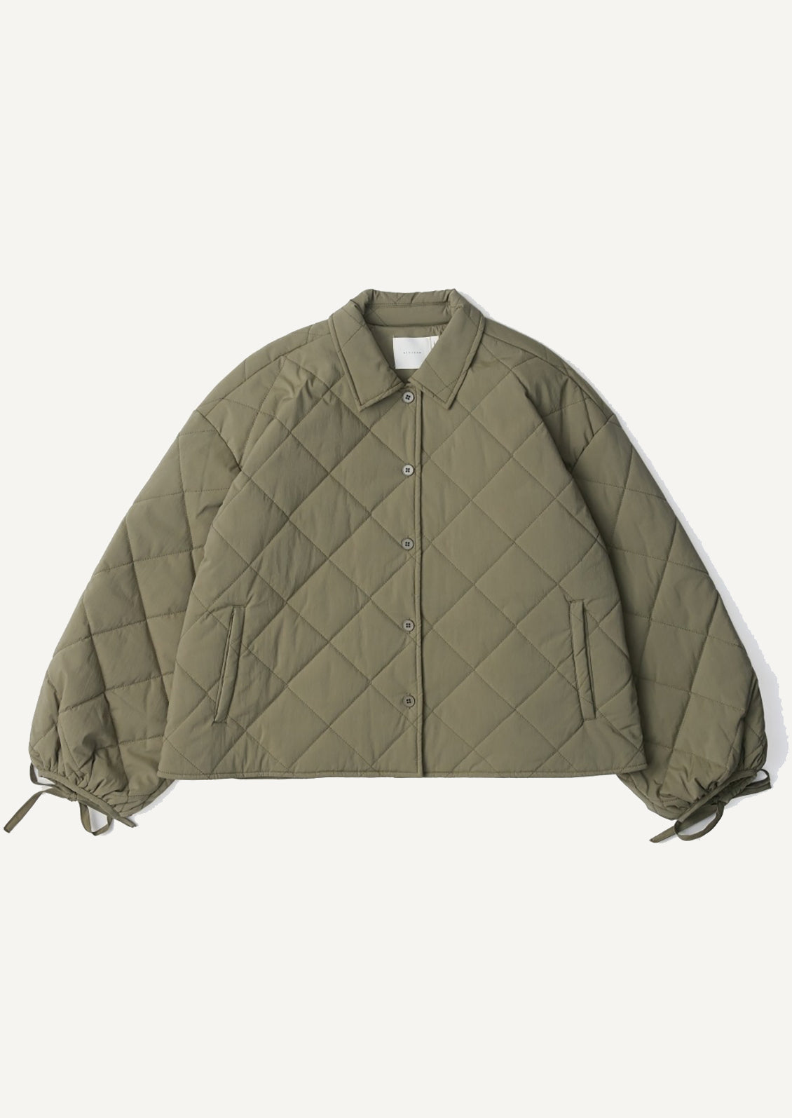 A woman wearing a quilted, padded jacket in army green with tie detail at wrists.