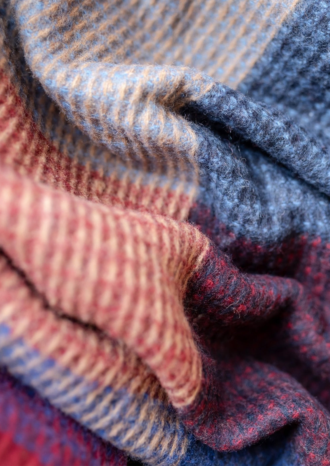 A colorblock grid print blanket with waffle texture in tones of red, cobalt blue and beige.