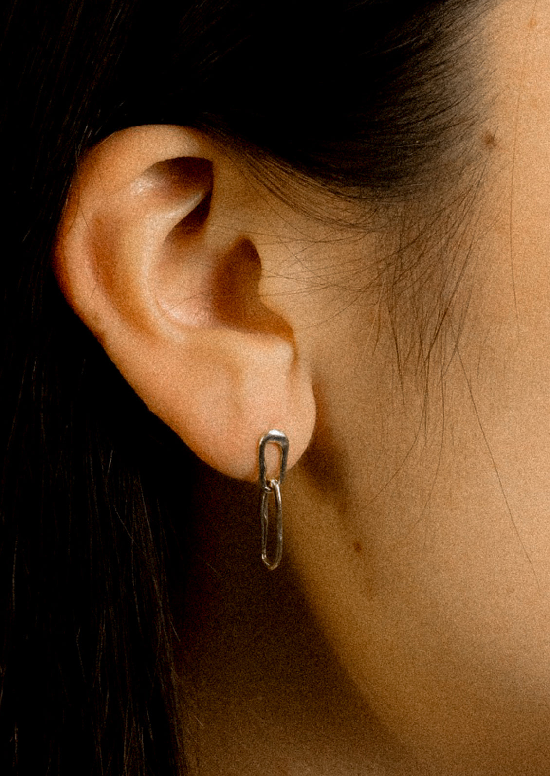 A person wearing a pair of tiny sterling silver earrings with two amorphous link shapes connected.