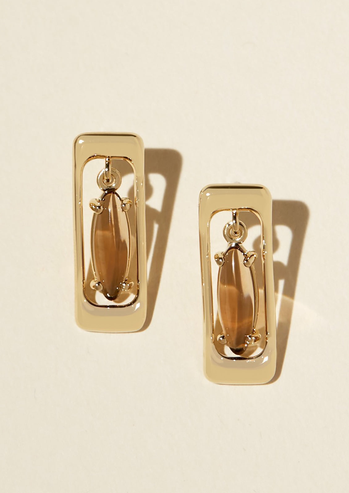 A pair of gold earrings in rectangular shape with pendulum brown baguette-cut gemstone at center.