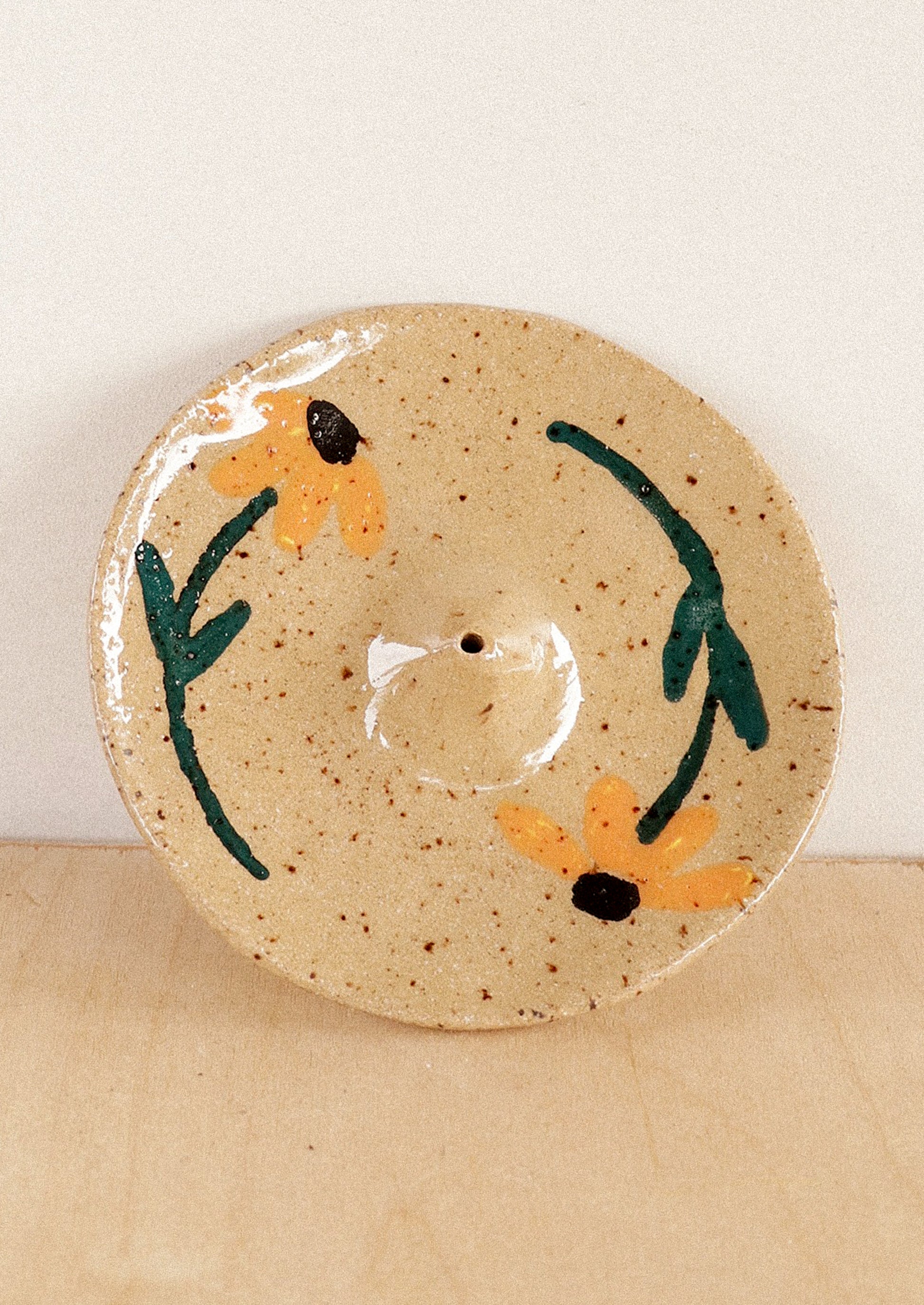 A speckled sand ceramic incense holder with hand painted sunflower design.
