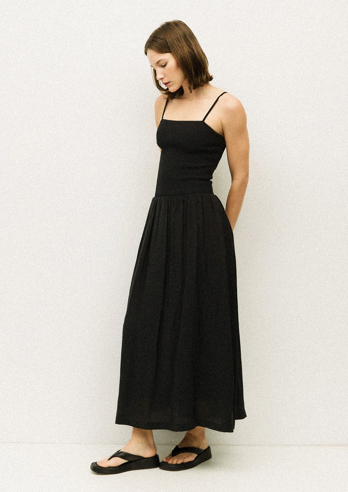 A woman wearing a black spaghetti strap dress with fitted bodice.