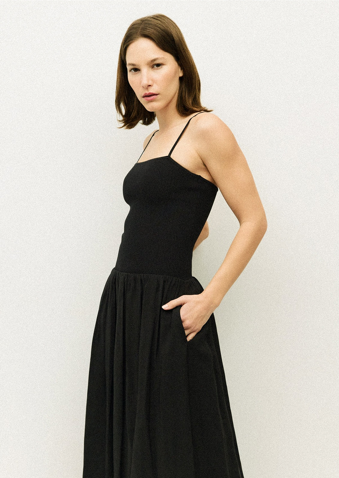 A woman wearing a black spaghetti strap dress with fitted bodice.