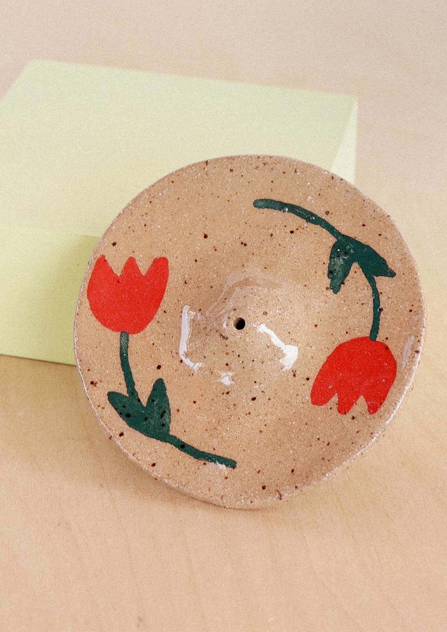 A speckled sand ceramic incense holder with hand painted red tulip design.