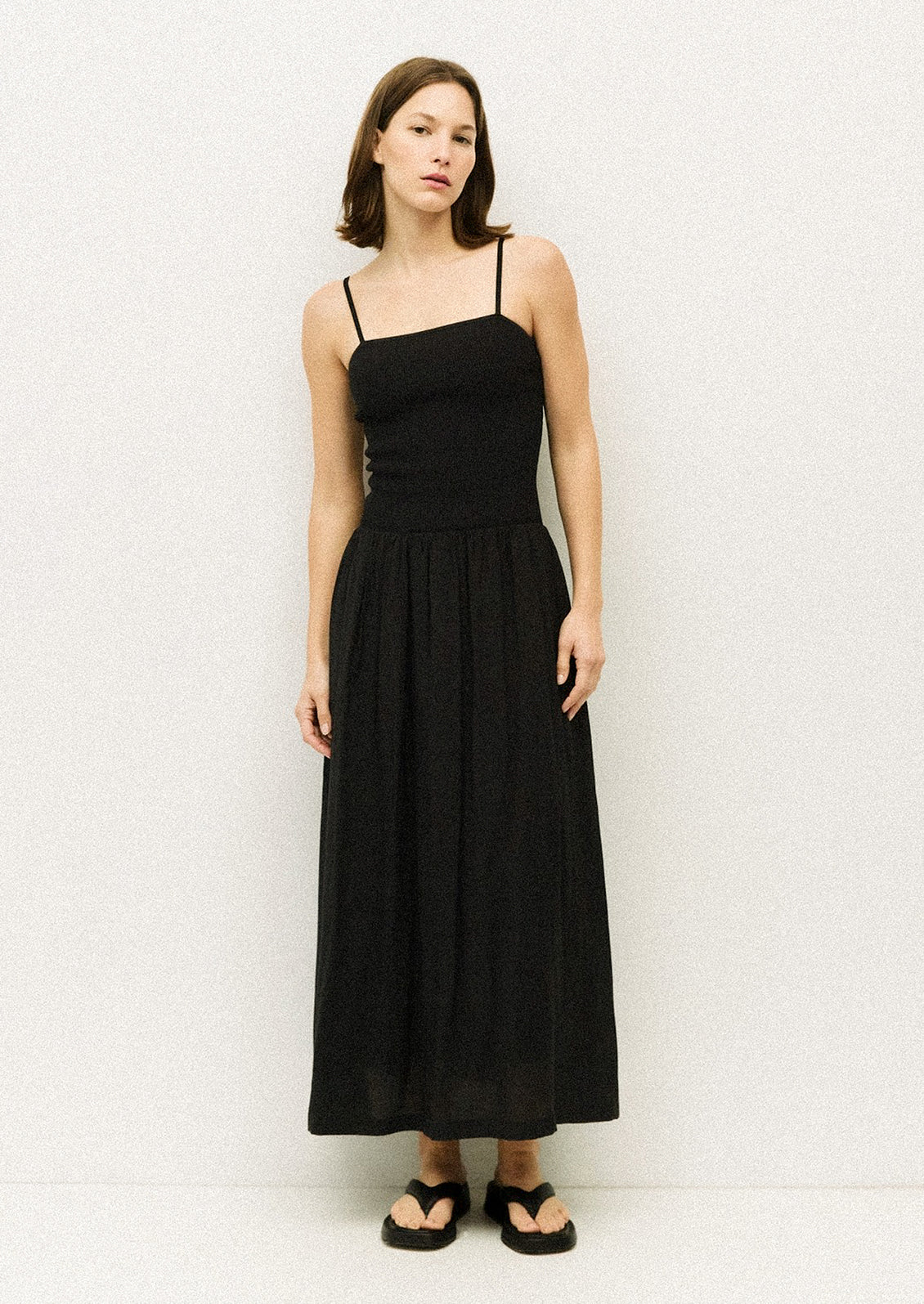 A woman wearing a black spaghetti strap dress with fitted bodice.