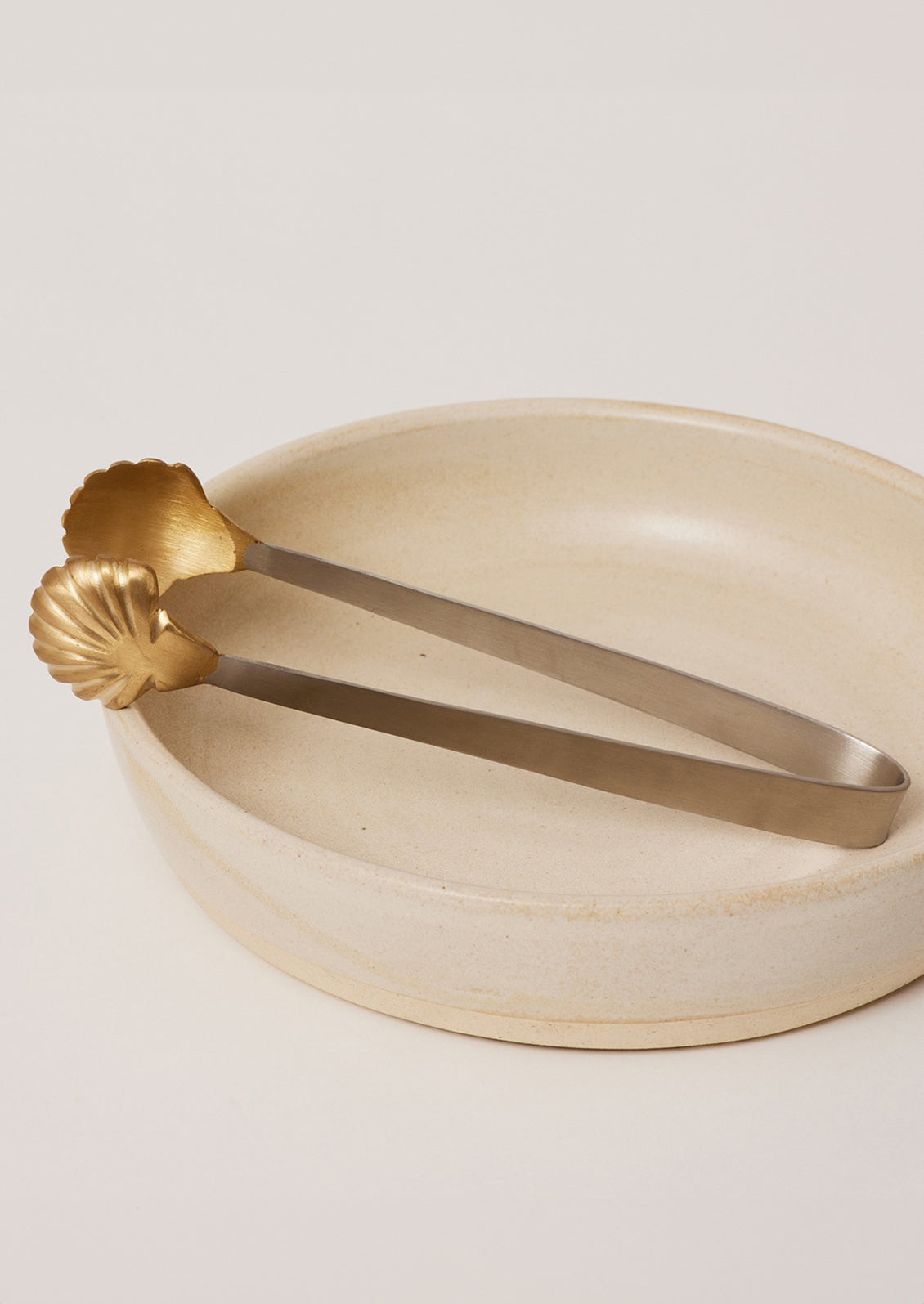 A pair of stainless steel serving tongs with brass seashell tip.