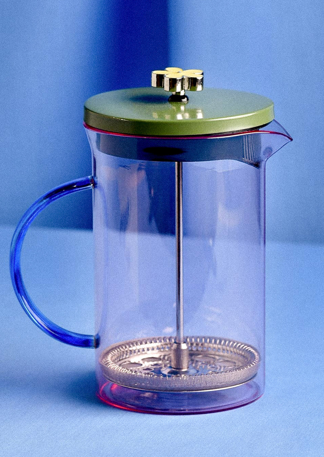 A pink glass french press with blue glass handle and green enameled lid with flower handle.