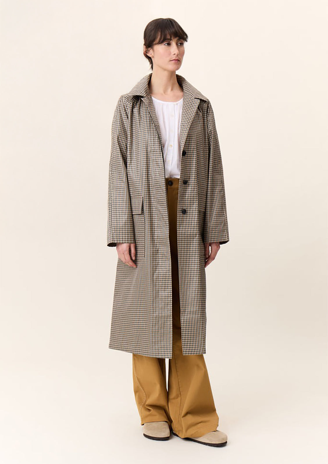A woman wearing a trench coat in small green and beige gingham pattern.
