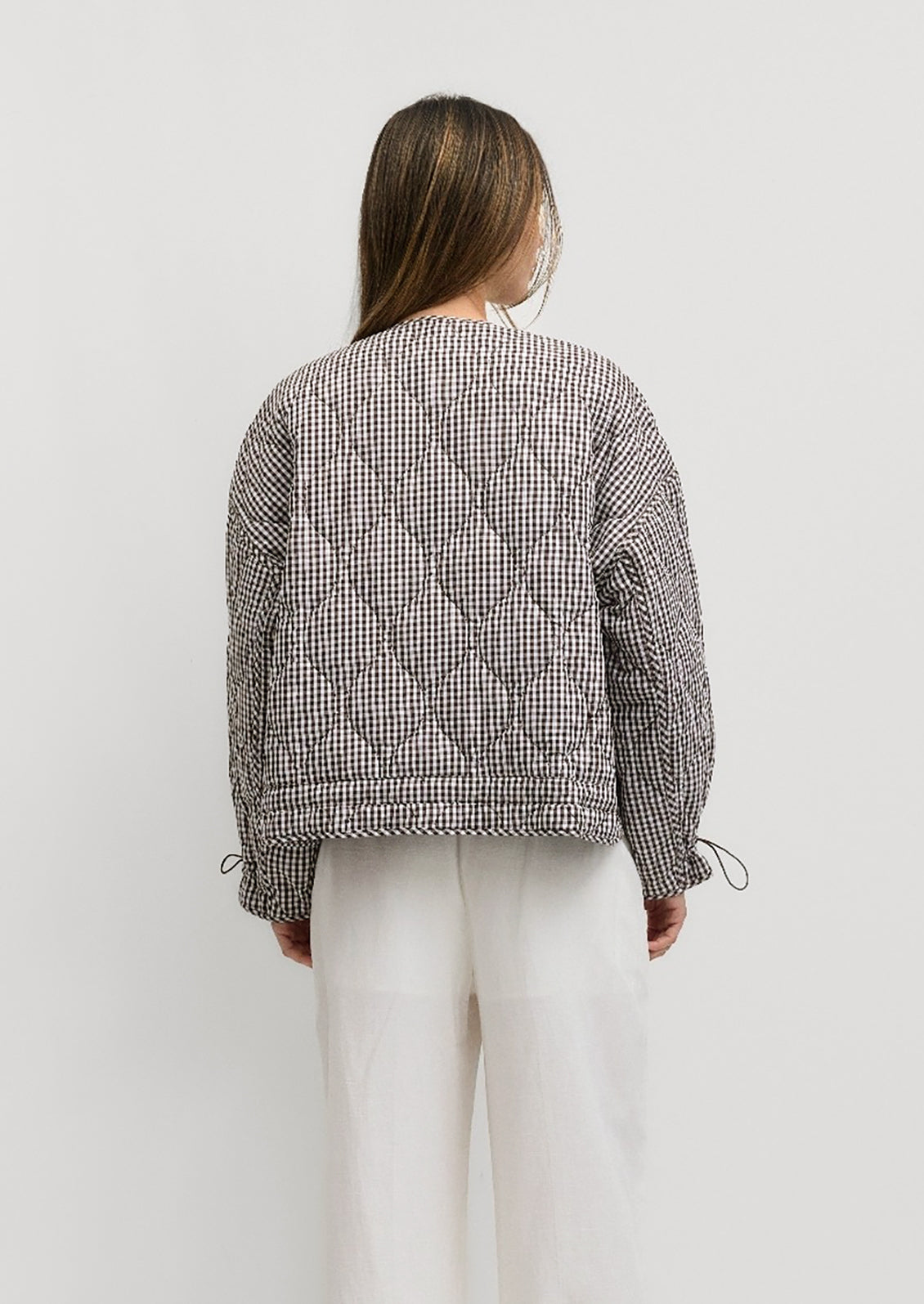 A woman wearing a quilted jacket in chocolate brown and white gingham.