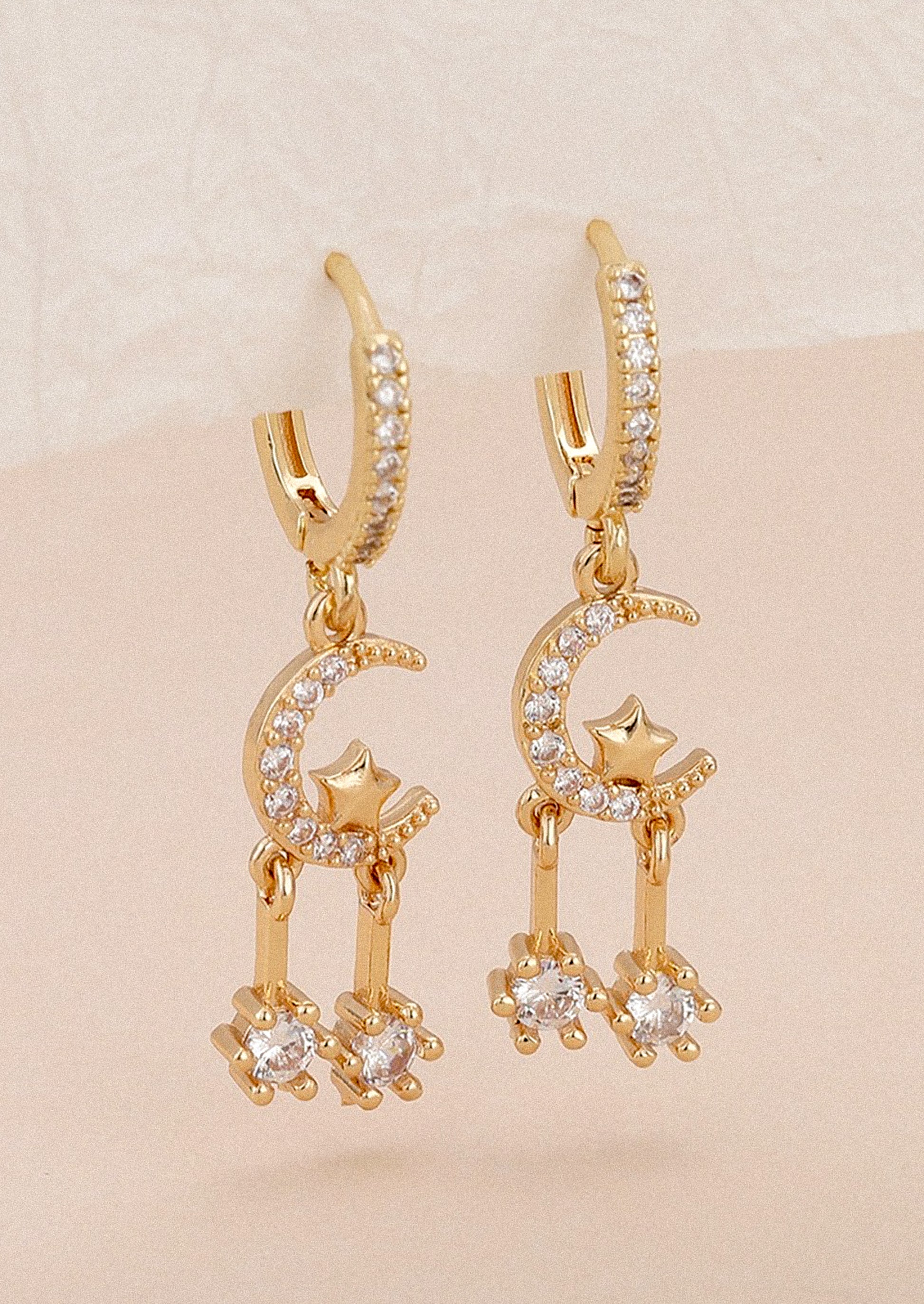 A pair of gold and clear crystal earrings with huggie hoop and moon and star crystal dangle charm.