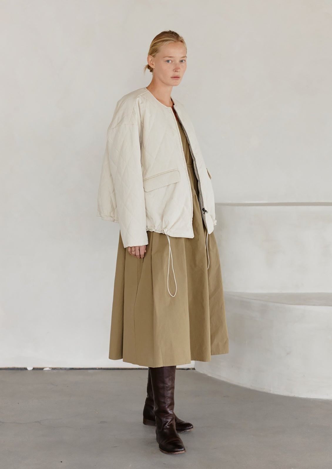 A woman wearing a padded quilted jacket with bottom drawstring detail in cream.