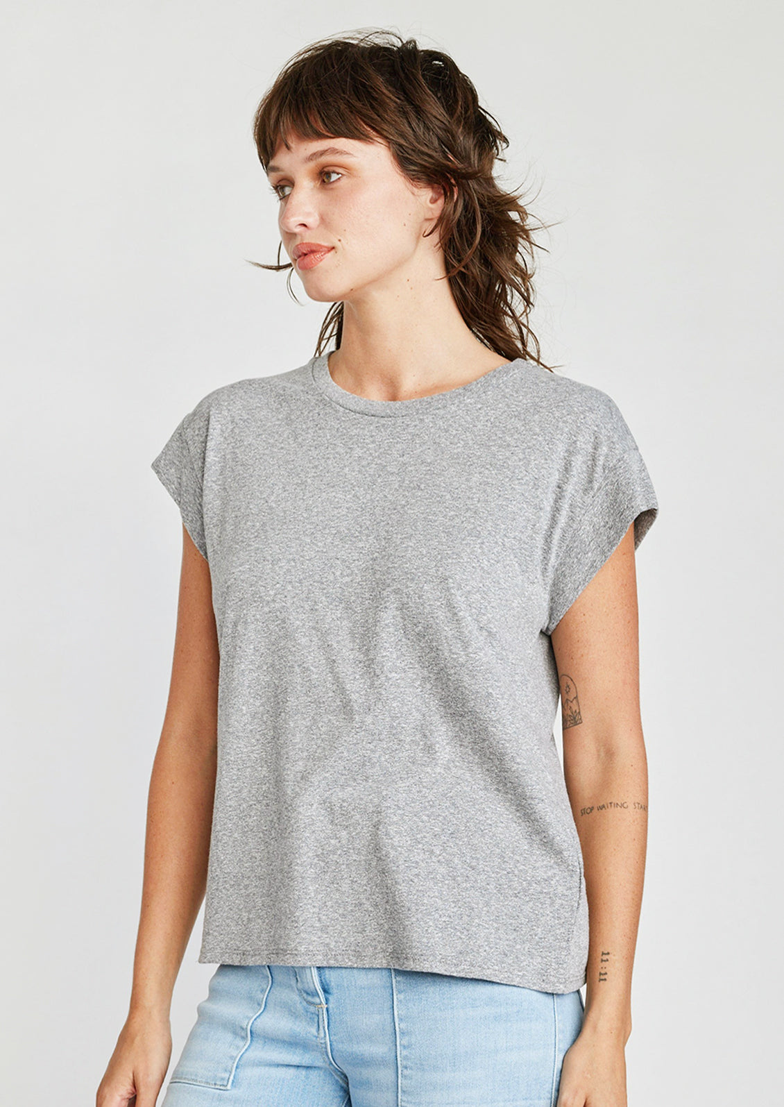 A woman wearing a cap sleeve muscle tee in heather grey color.