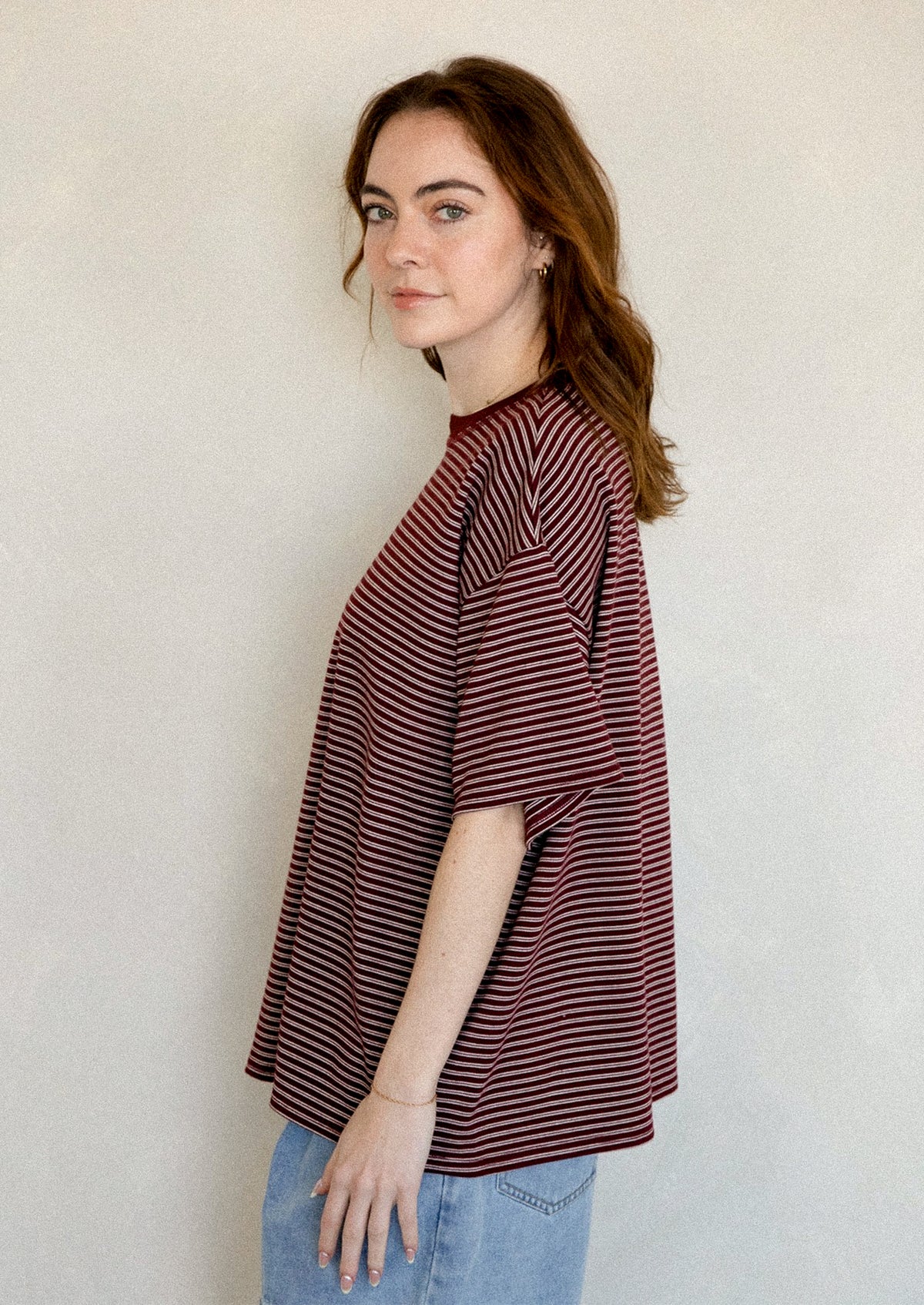 A person wearing an oversized t-shirt in maroon with white stripes.