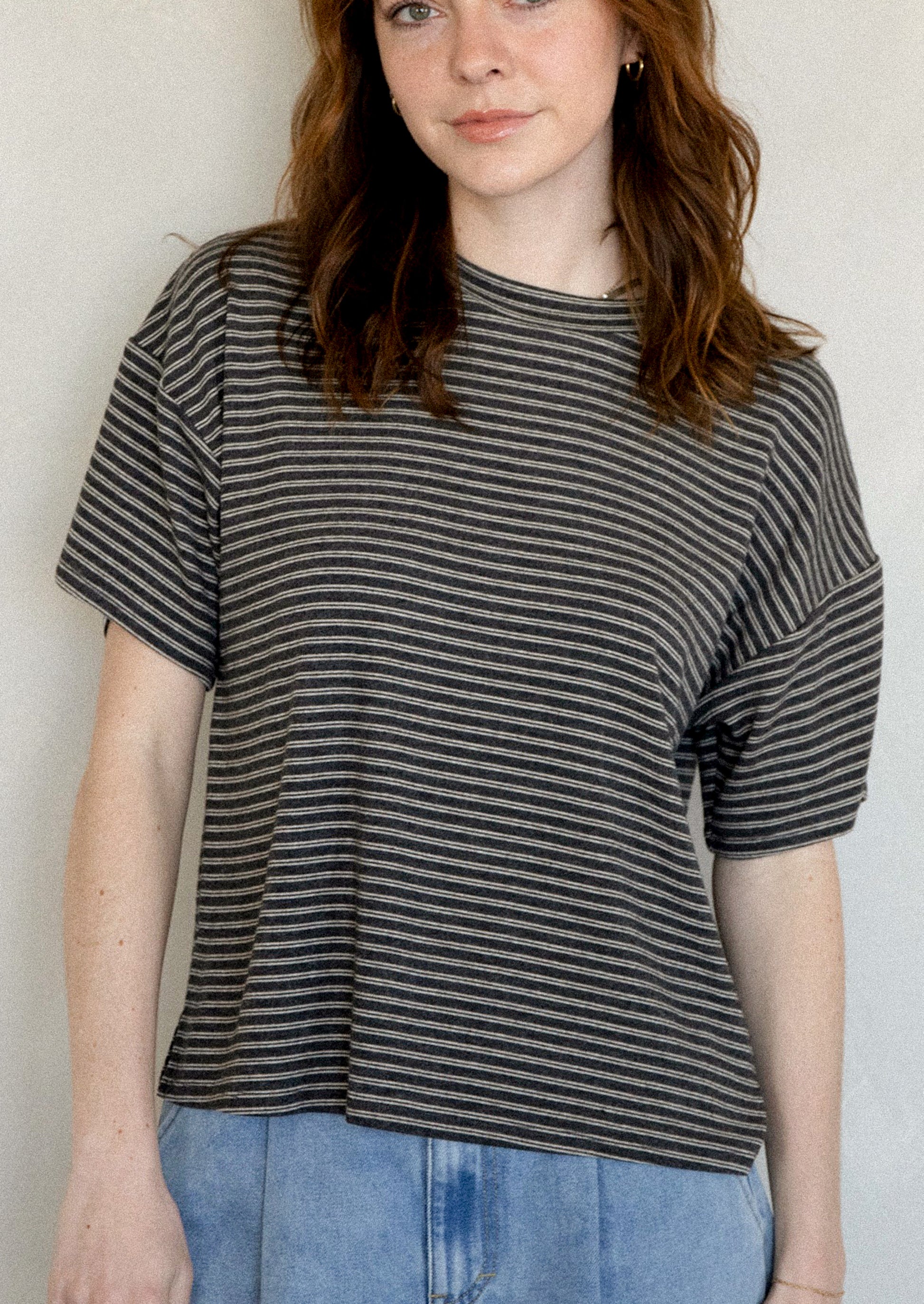 A woman wearing a slouchy t-shirt in charcoal with thin white stripes.