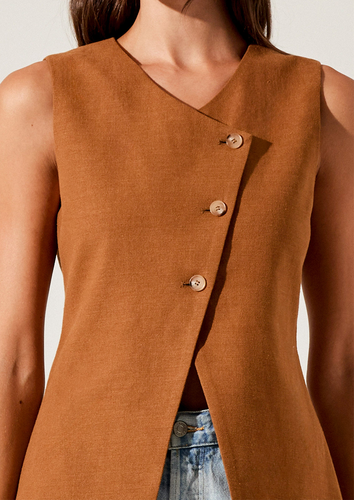 A person wearing a rust colored vest with asymmetrical button front closure.