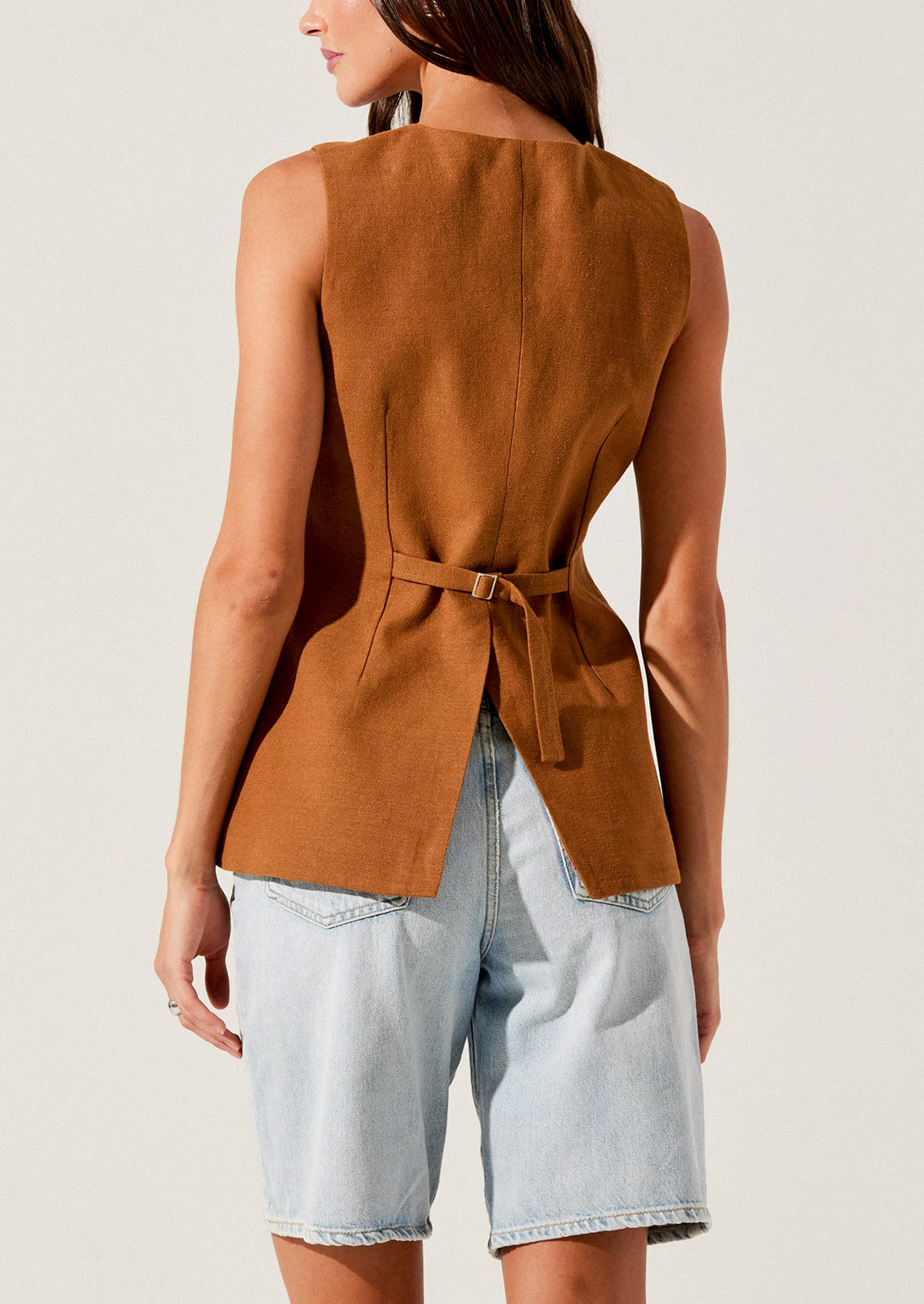A person wearing a rust colored vest with asymmetrical button front closure.