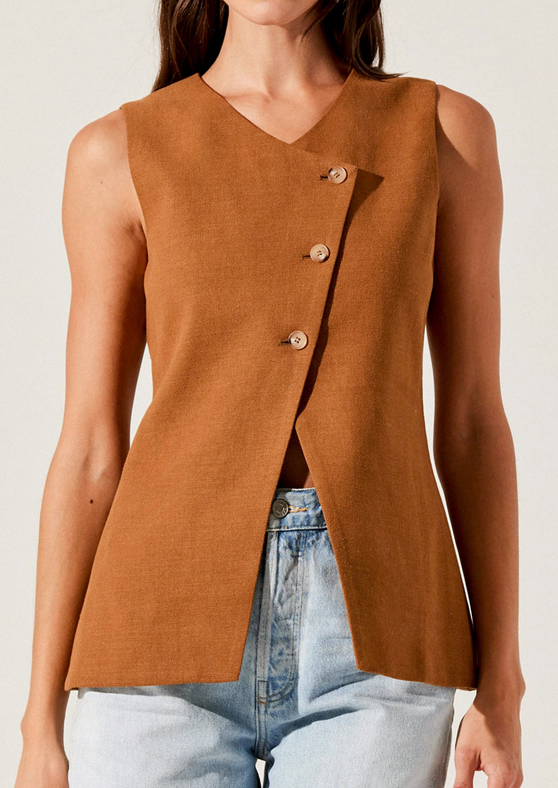 A person wearing a rust colored vest with asymmetrical button front closure.