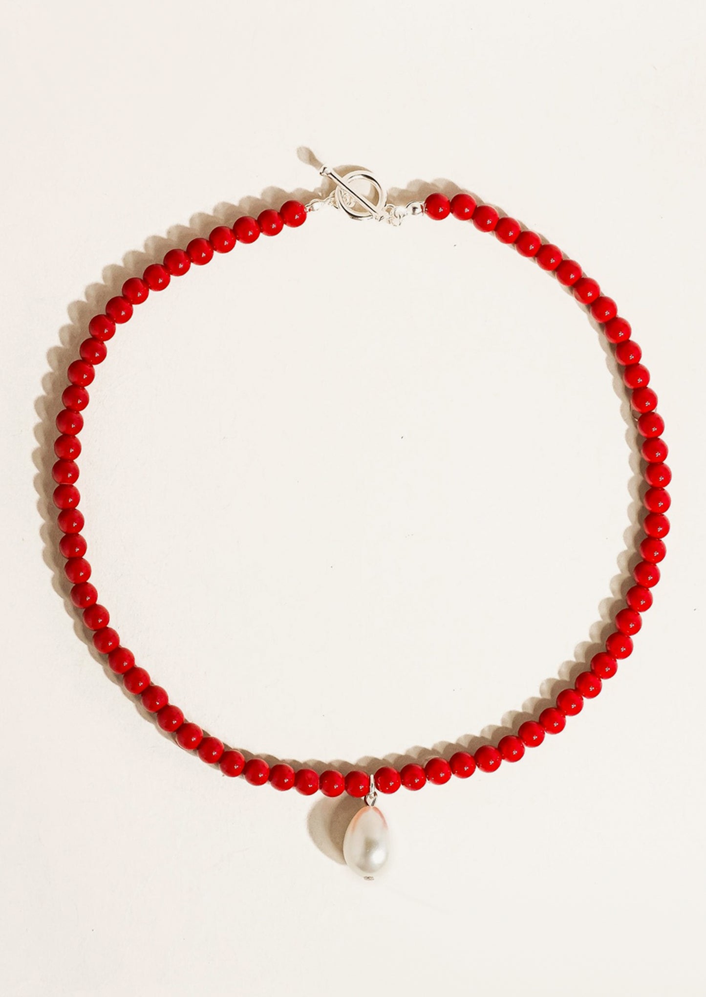 A red beaded necklace with silver hardware and pearl charm.