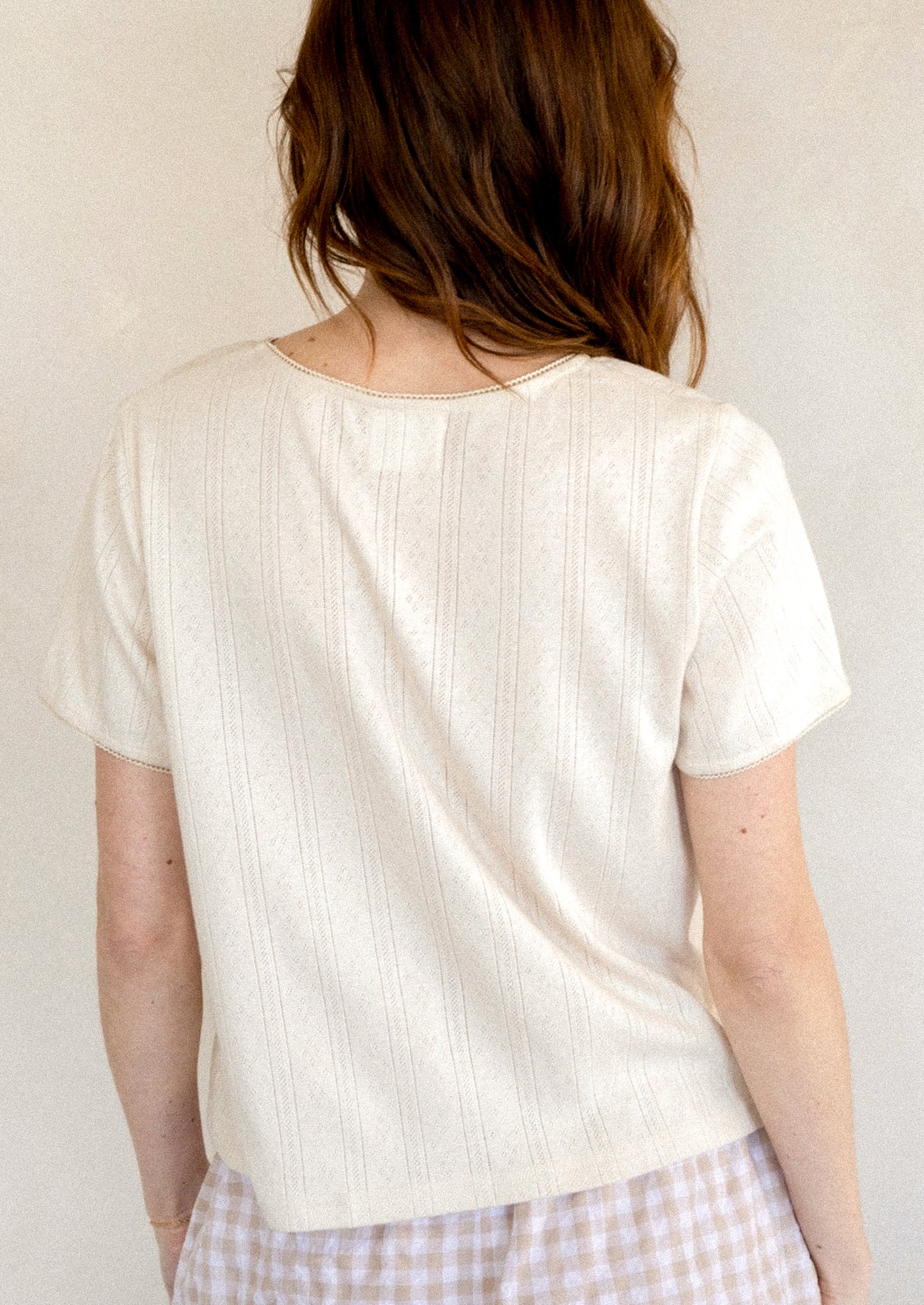 A woman wearing a pointelle stitch tee in cream.