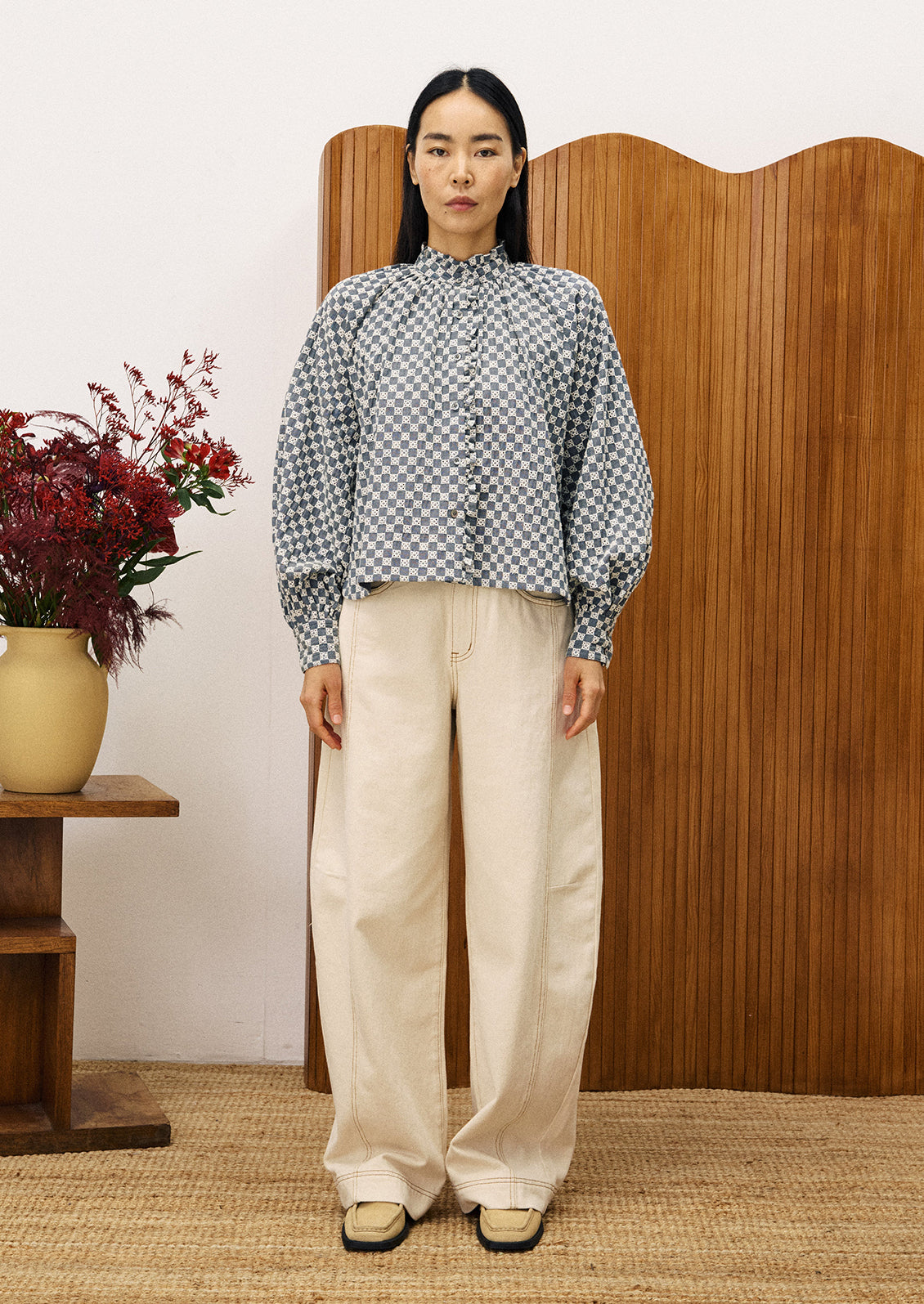 A woman wearing a ruffle neck blouse with embroidered white check pattern.