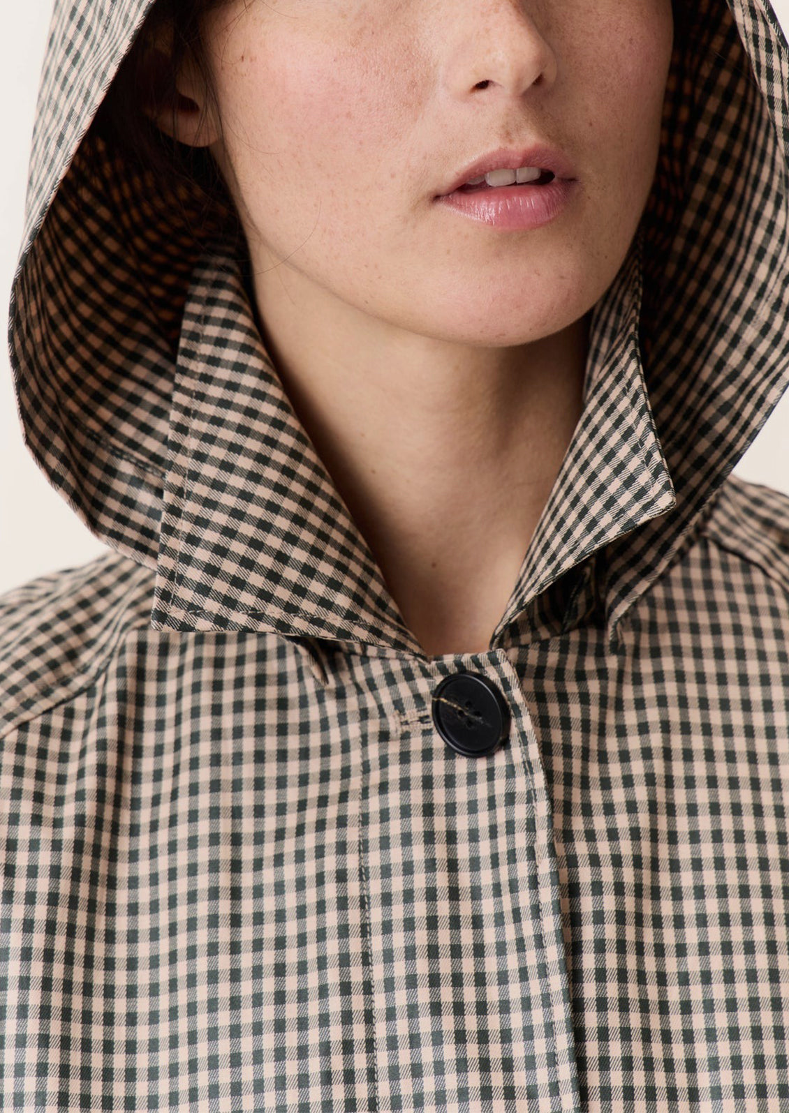 A woman wearing a trench coat in small green and beige gingham pattern.