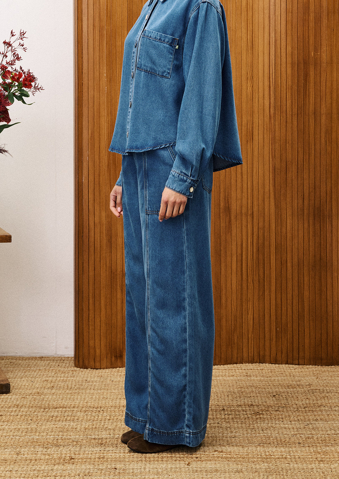 Person wearing a blue denim outfit standing against a wooden wall.