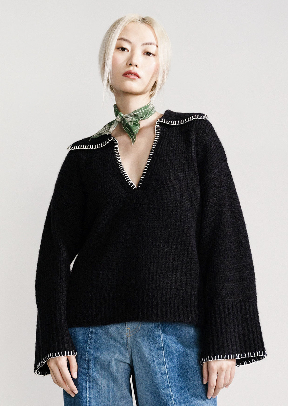 A woman wearing a black sweater with notched collared v-neckline and wide bell sleeves.