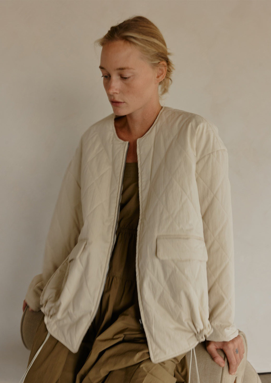 A woman wearing a padded quilted jacket with bottom drawstring detail in cream.