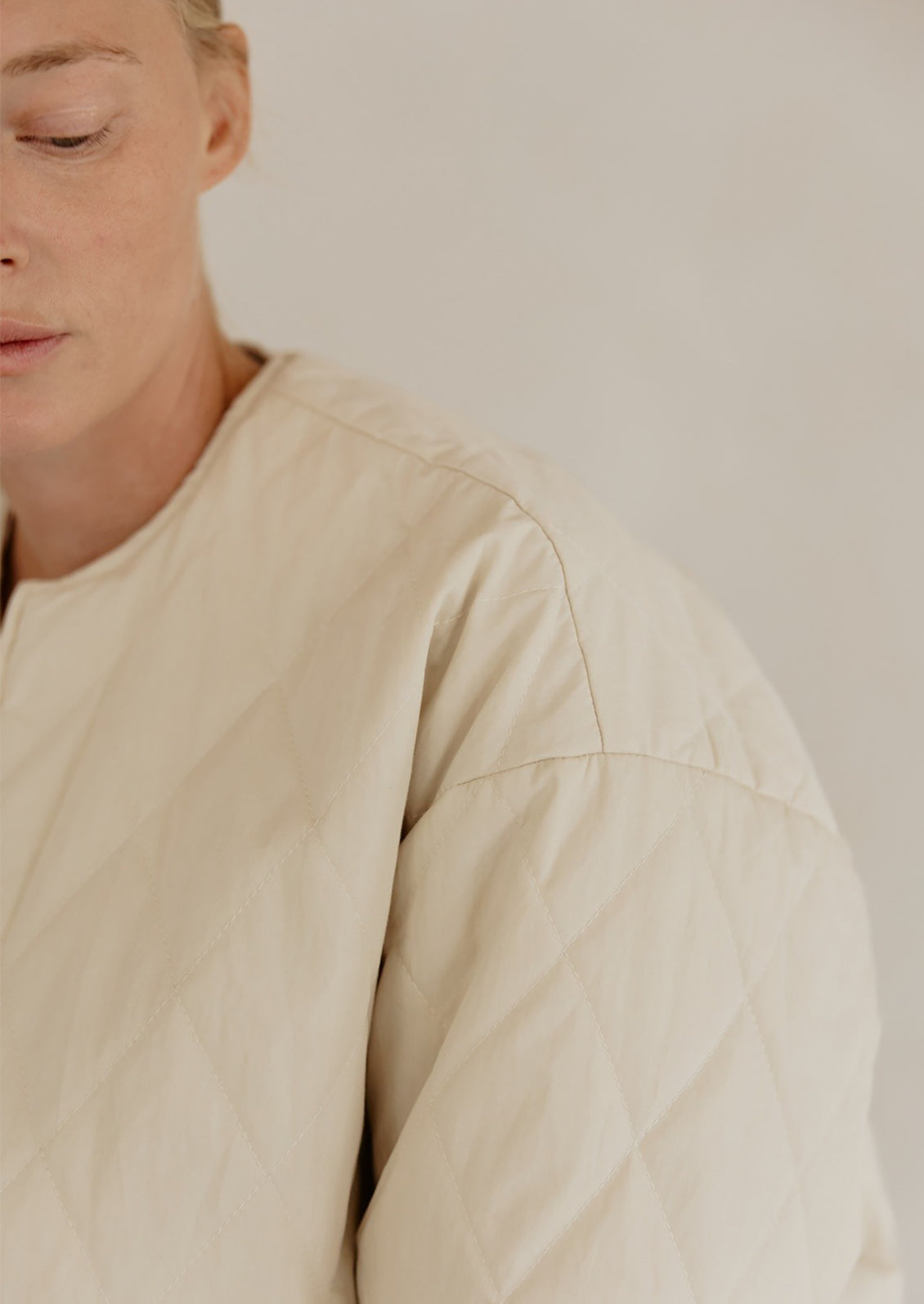A woman wearing a padded quilted jacket with bottom drawstring detail in cream.