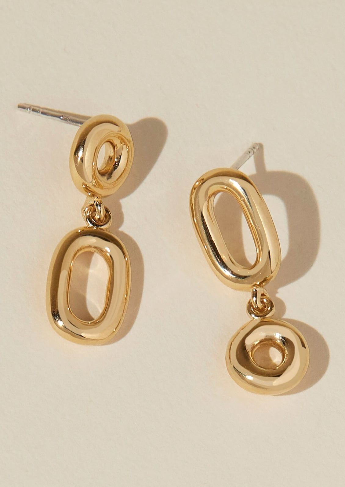 A pair of gold earrings with hollow circle and oval shapes.