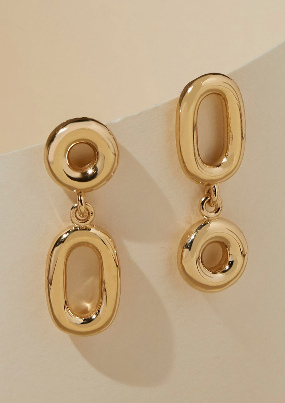 A pair of gold earrings with hollow circle and oval shapes.