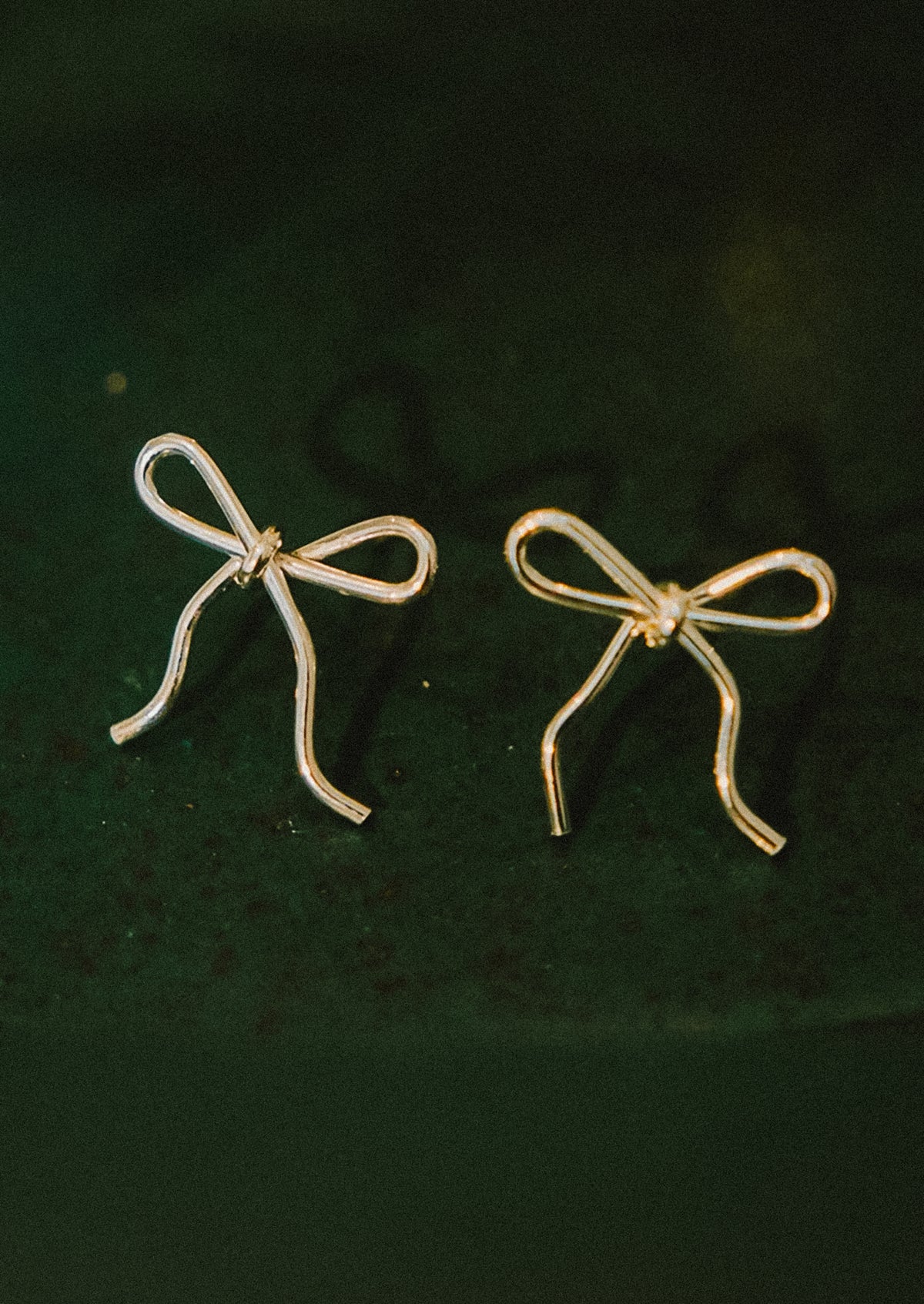 A pair of small handmade earrings in bow shape made from gold wire.