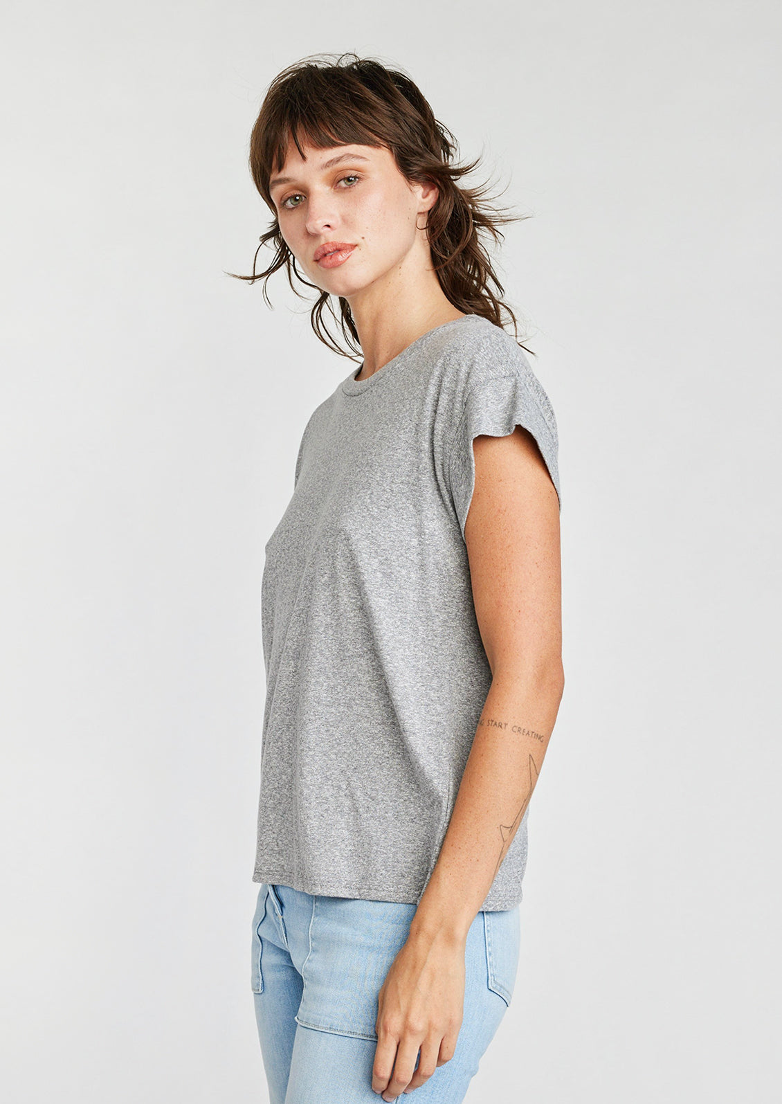 A woman wearing a cap sleeve muscle tee in heather grey color.