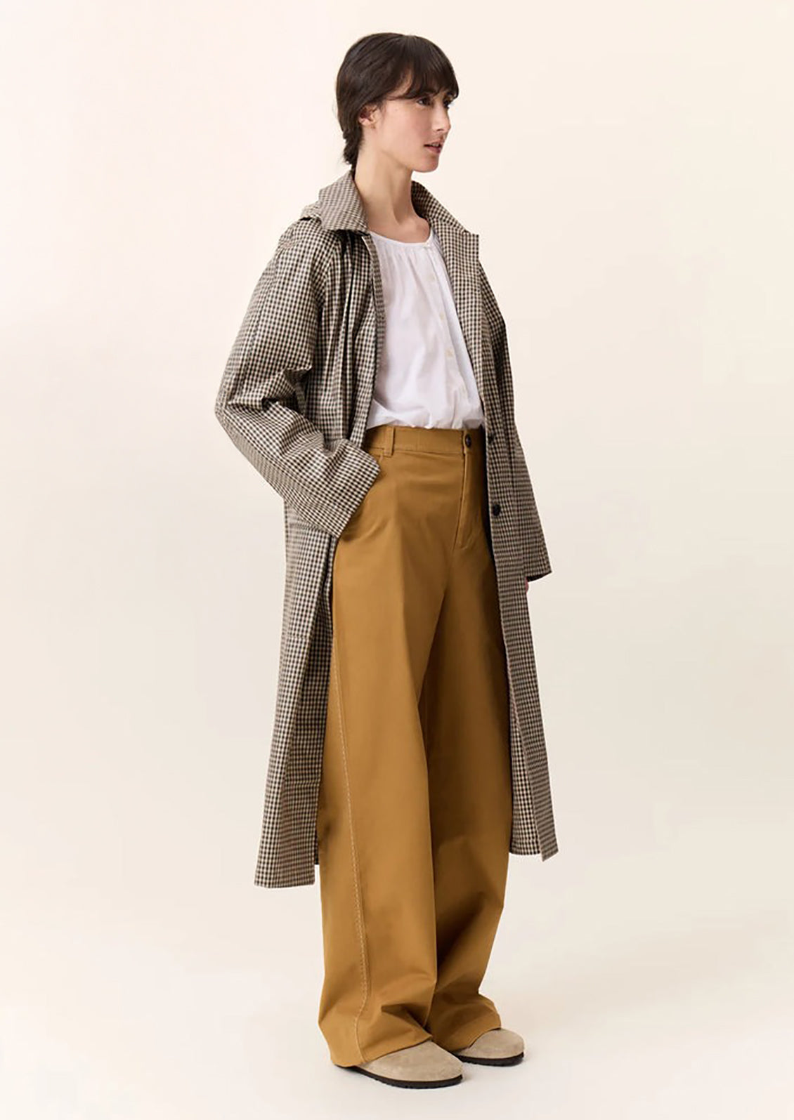 A woman wearing a trench coat in small green and beige gingham pattern.